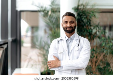 Portrait of an Indian general medicine doctor, stands with arms crossed in a clinic, dressed in medical clothes with a stethoscope around his neck, looking at camera, smiling friendly. Medical expert - Powered by Shutterstock