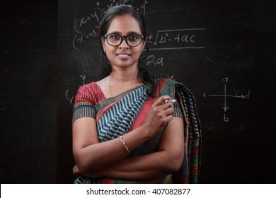 Portrait Of Indian Lady Teacher Stands In Front Of A Blackboard