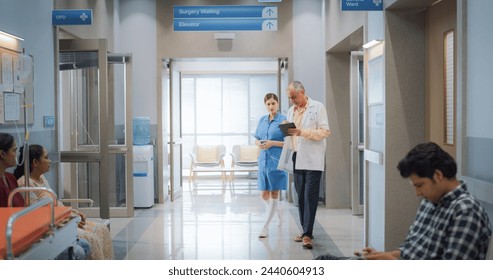Portrait of Indian Male Doctor and Female Nurse Walking in Hospital Corridor and Talking while Using a Digital Tablet. Medical Specialists Sharing Notes and Instructions