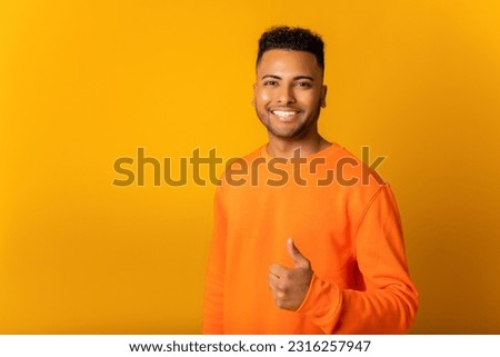 Portrait of indian man standing with thumb up, like gesture, demonstrating approval and agree with suggestion. Indoor studio shot isolated on orange background