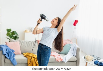 Portrait of Indian teenage girl dancing and singing karaoke, using blowdryer as microphone, having domestic concert. Cute adolescent having fun, performing popular song at home