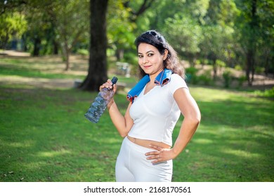 Portrait Of Indian Woman Athlete Takes A Break Holding Water Bottle Wearing White Cloths, Asian Female Standing On A Hot Day In The Park.