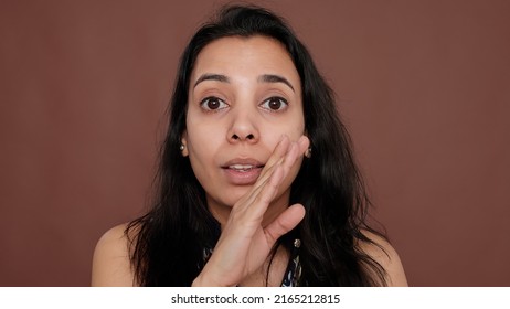 Portrait of indian woman sharing overheard secret in studio, spreading confidential information as rumor, being nosy. Telling secret about someone, unbelievable gossip from private conversation.