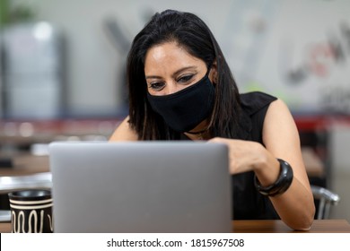 Portrait Of An Indian Woman Wearing Covid 19 Protection Mask And Working On Her Laptop, Sitting In An Office Cafeteria, Coffee Shop, Casual Work Environment.