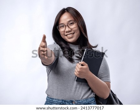 Portrait of an Indonesian Asian woman, wearing a gray dress, posing ready to go to campus with books and a bag, isolated against a white background.