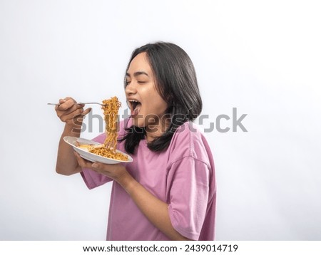 Portrait of an Indonesian Asian woman, wearing a pink shirt, happily eating instant noodles, isolated against a white background.