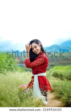 Portrait of an Indonesian woman, wearing a red Balinese kebaya. Take a photo with a rice field background.