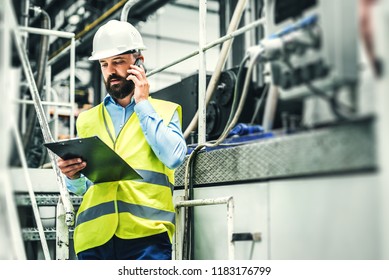 A portrait of an industrial man engineer with smartphone in a factory, working. - Powered by Shutterstock