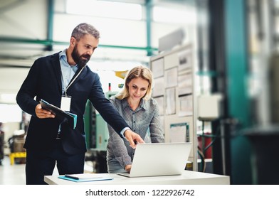 A Portrait Of An Industrial Man And Woman Engineer With Laptop In A Factory, Working.