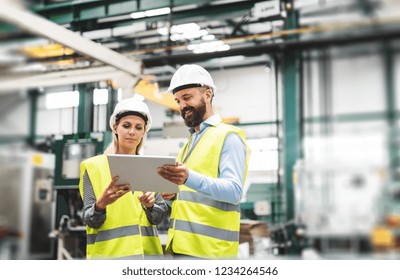 A Portrait Of An Industrial Man And Woman Engineer With Tablet In A Factory, Talking.