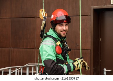 Portrait Industrial Mountaineering Worker In Uniform On Roof Residential Facade Building During High-rise Work Outdoors. Rope Access Laborer On Roof Of House. Concept Of Industry Urban Works