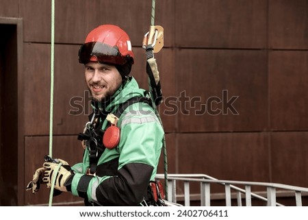 Portrait industrial mountaineering worker in uniform on roof residential facade building during high-rise work outdoors. Rope access laborer on roof of house. Concept of industry urban works