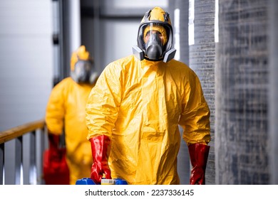 Portrait of industrial worker in hazmat protection suit and gas mask working inside chemicals production plant. In background large tanks with acid and factory interior.