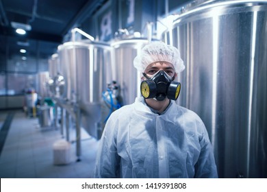 Portrait Of Industrial Worker Technologist Wearing Hazmat Suit In Production Plant. Man In White Protective Uniform With Hairnet And Protective Mask Handling Hazardous Chemicals.