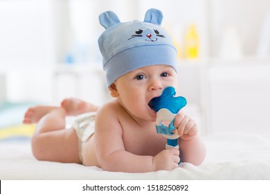 Portrait Of Infant Baby Boy Weared Funny Hat. Kid Lying On Bed And Playing With Teething Toy