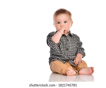 Portrait of infant child baby boy toddler with dark blue eyes dressed in beige pants and a checkered shirt. Child sits barefoot and happily smiles on a white background with space for text.
