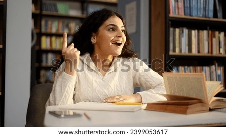 Portrait of inspired young pretty woman student searching inspiration and find solution idea answer with raised finger sitting at desk in university library 