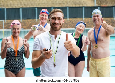 Portrait of instructor and senior swimmers showing thumbs up at poolside - Powered by Shutterstock