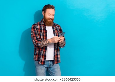 Portrait of intelligent man with cool tattoo wear plaid shirt look at smartphone write email isolated on blue color background - Powered by Shutterstock
