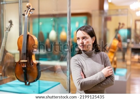 Portrait of interested adult brunette visiting exhibition of medieval musical instruments in historical museum ..