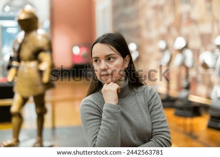 Portrait of interested adult female tourist visiting exhibition of medieval armor in armory of historical museum ..