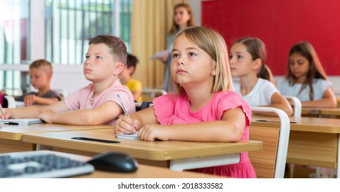 Portrait Of Interested Blonde Tween Girl Studying In Classroom, Listening To Schoolteacher And Writing In Notebook