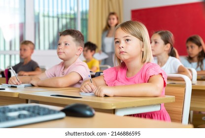 Portrait Of Interested Blonde Tween Girl Studying In Classroom, Listening To Schoolteacher And Writing In Notebook