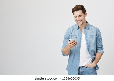 Portrait of interesting and handsome european man holding telephone while texting, isolated over white background. Person is laughing at meme his friend sent to him, answering with funny emoji