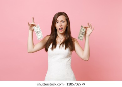 Portrait Of Irritated Sad Bride Woman In Lace White Wedding Dress Holding One Dollar Bills Isolated On Pastel Pink Background. Lack Of Money. Organization Of Wedding Celebration Concept. Copy Space