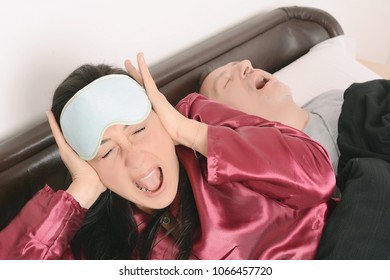 Portrait of irritated woman blocking ears with hands while man snoring on bed. Indoors - Powered by Shutterstock