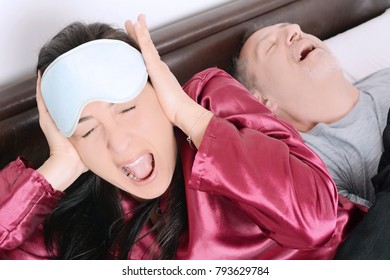 Portrait of irritated woman blocking ears with hands while man snoring on bed. Indoors - Powered by Shutterstock