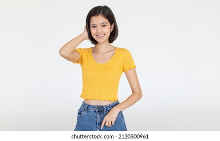 Portrait Isolated Cutout Studio Shot Of Asian Pretty Friendly Young Teenager Short Hair Girl Model In Casual Crop Top Shirt And Jeans Standing Posing Holding Hand On Head Smiling On White Background.