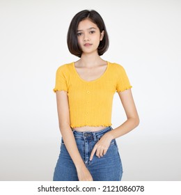 Portrait Isolated Cutout Studio Shot Of Asian Pretty Friendly Young Teenager Short Hair Girl Model In Casual Crop Top Shirt And Jeans Standing Posing Holding Hand On Head Smiling On White Background.