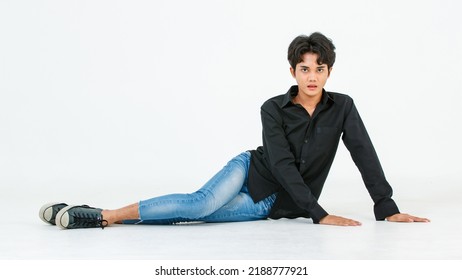 Portrait Isolated Cutout Studio Shot Of Asian Young LGBTQ Gay Glamour Male Model In Casual Black Shirt And Jeans Outfit Sitting Stretching Posing Gesturing On Floor Look At Camera On White Background.