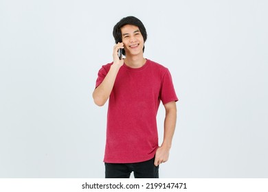 Portrait Isolated Cutout Studio Shot Of Asian Young Handsome Teenager Male Model In Street Style Outfit Standing Holding Smartphone In Hands Smiling Taking Selfie Photo On White Background.