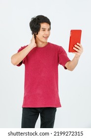 Portrait Isolated Cutout Studio Shot Of Asian Young Handsome Teenager Male Model In Street Style Outfit Standing Holding Tablet Computer In Hands Smiling Taking Selfie Photo On White Background.