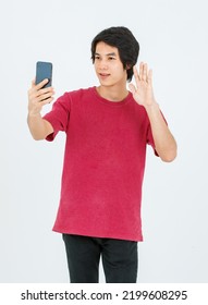 Portrait Isolated Cutout Studio Shot Of Asian Young Handsome Teenager Male Model In Street Style Outfit Standing Holding Smartphone In Hands Smiling Taking Selfie Photo On White Background.