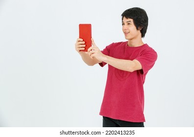 Portrait Isolated Cutout Studio Shot Of Asian Young Handsome Teenager Male Model In Street Style Outfit Standing Holding Tablet Computer In Hands Smiling Taking Selfie Photo On White Background.