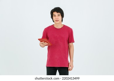 Portrait Isolated Cutout Studio Shot Of Asian Young Handsome Teenager Male Model In Street Style Outfit Standing Holding Tablet Computer In Hands Smiling Taking Selfie Photo On White Background.