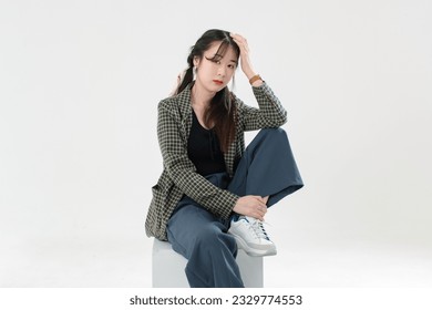 Portrait isolated cutout studio shot Asian young pretty female fashion model with pigtails braids hair in casual plaid suit crop top shirt sitting on square box posing look camera on white background - Shutterstock ID 2329774553