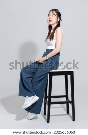 Portrait isolated cutout studio shot Asian young pretty female fashion model with pigtails braids hair in fashionable sleeveless crop top sitting on tall chair posing look camera on white background.