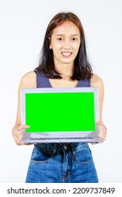 Portrait Isolated Studio Cutout Shot Of Asian Female Model Smiling Look At Camera Holding Pointing Green Blank Screen Laptop Computer Showing Product Promotion Advertisement On White Background.