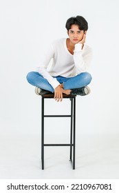 Portrait Isolated Studio Shot Asian Young LGBT Gay Happy Handsome Bisexual Homosexual Male Fashion Model In Casual Outfit Sitting Crossed Legs On Tall Chair Smiling Look At Camera On White Background.