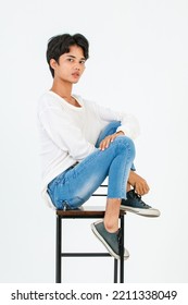 Portrait Isolated Studio Shot Asian Young LGBT Gay Happy Handsome Bisexual Homosexual Male Fashion Model In Casual Outfit Sitting Crossed Legs On Tall Chair Smiling Look At Camera On White Background.