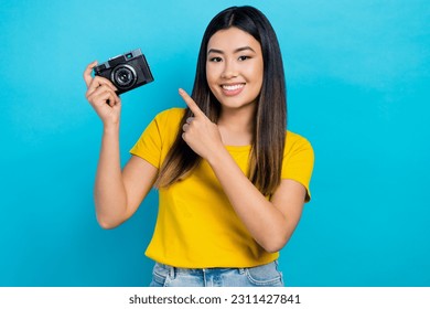 Portrait of japanese girl black hair wear t-shirt direct finger retro vintage photo camera new lens isolated on blue color background - Powered by Shutterstock