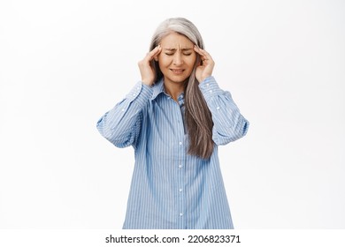 Portrait of japanese senior woman having headache, touching head and grimacing from pain, migraine, standing over white background. - Powered by Shutterstock