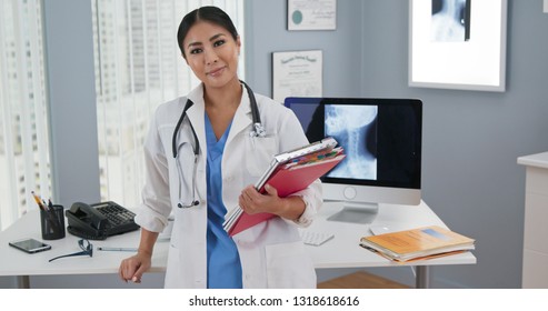 Portrait Of Japanese Woman Doctor Standing At Her Desk Looking At Camera. Medium Shot Of Confident Asian Female Physician