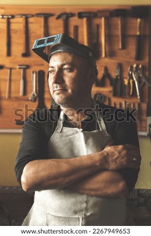 portrait of a jeweler craftsman in front of his tools looking confident at the window of his workshop wearing welding glasses. High quality photo