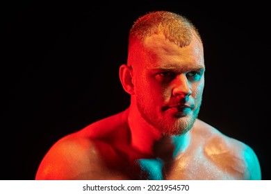 Portrait of jock sweating from training on black background in multicolour lighting. Side view. Male beauty concept. 