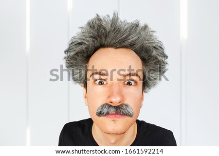 Portrait of jocular aging guy with grey long hair sticking his tongue out in Einstein manner